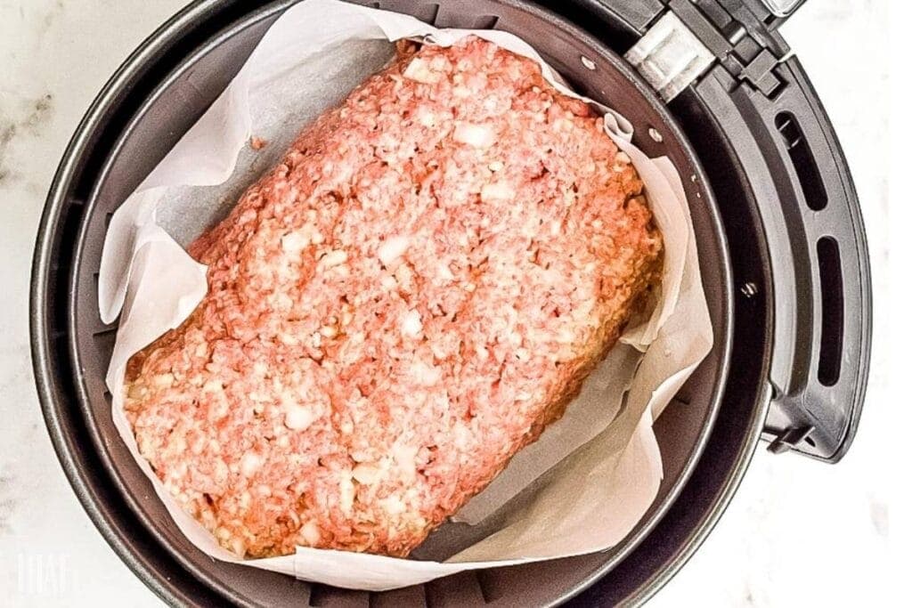 raw shaped meatloaf on parchment paper in air fryer basket