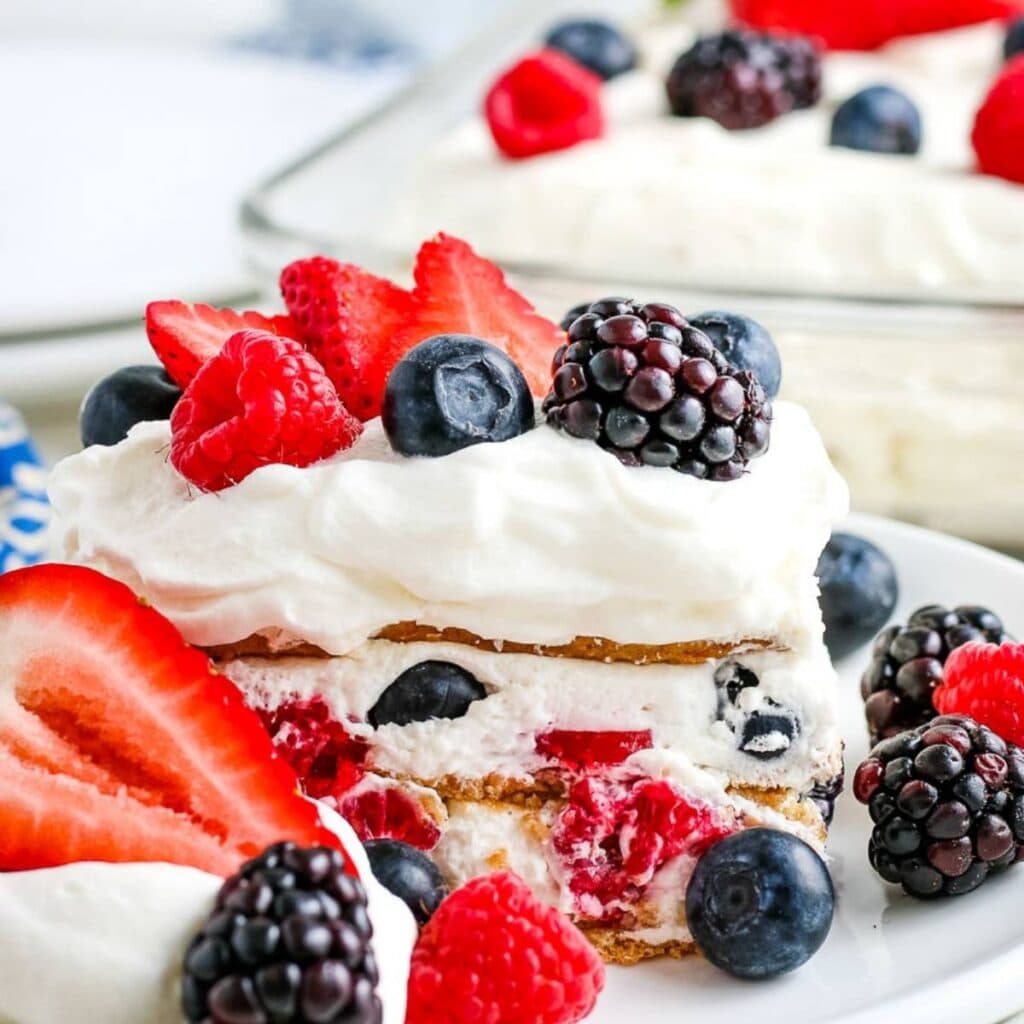 Closeup view of a slice of mixed berry icebox cake on a white plate with pan in the background.