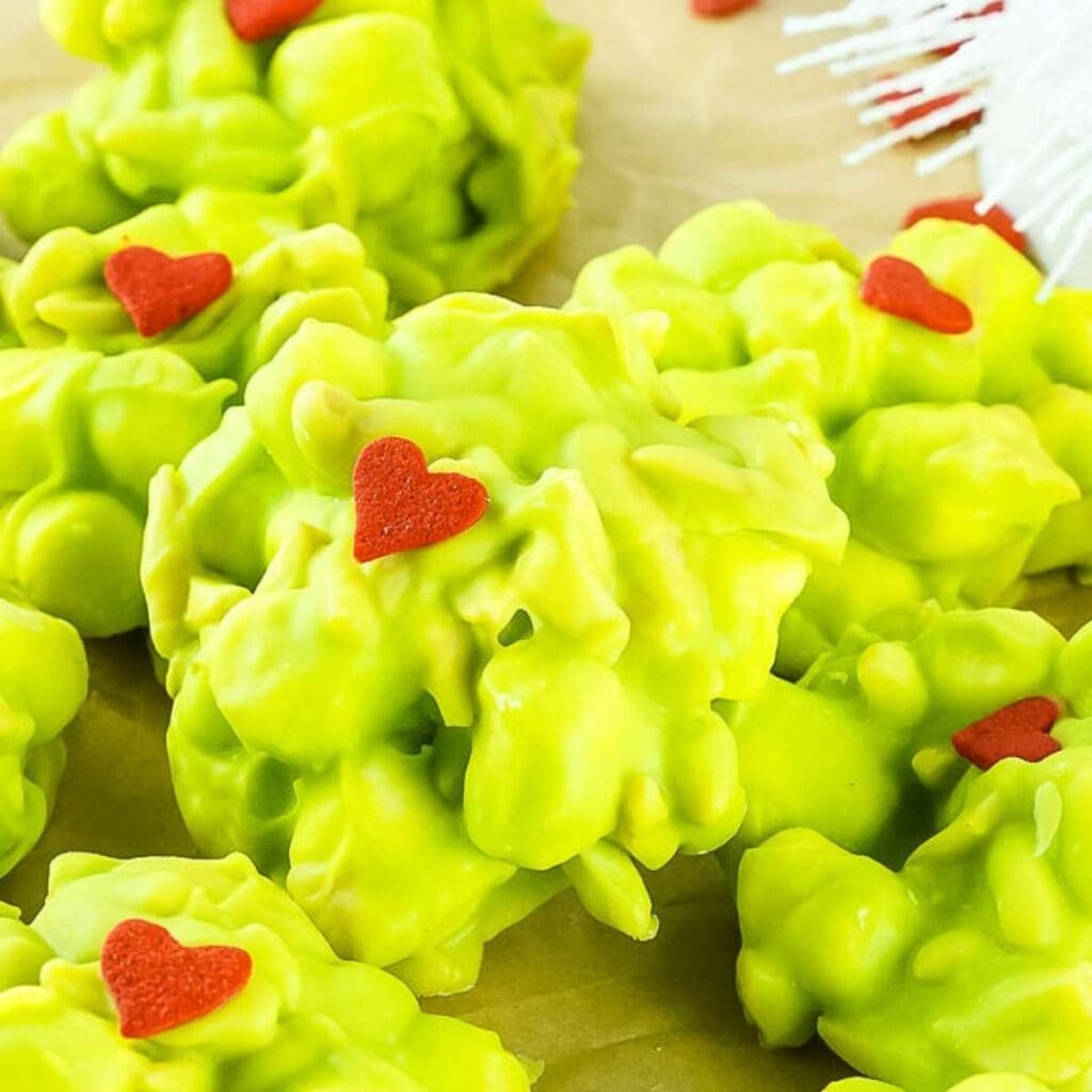 Close up of a Grinch rocky road candy with a small red heart on top and surrounded by more candy clusters.