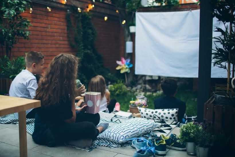 A family watching an outdoor movie with pillows and blankets.