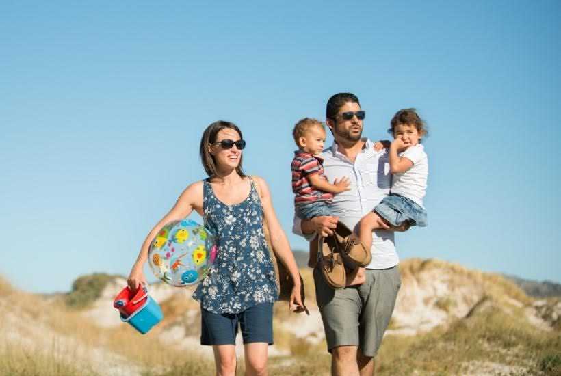 A family walking down to the beach with toys.