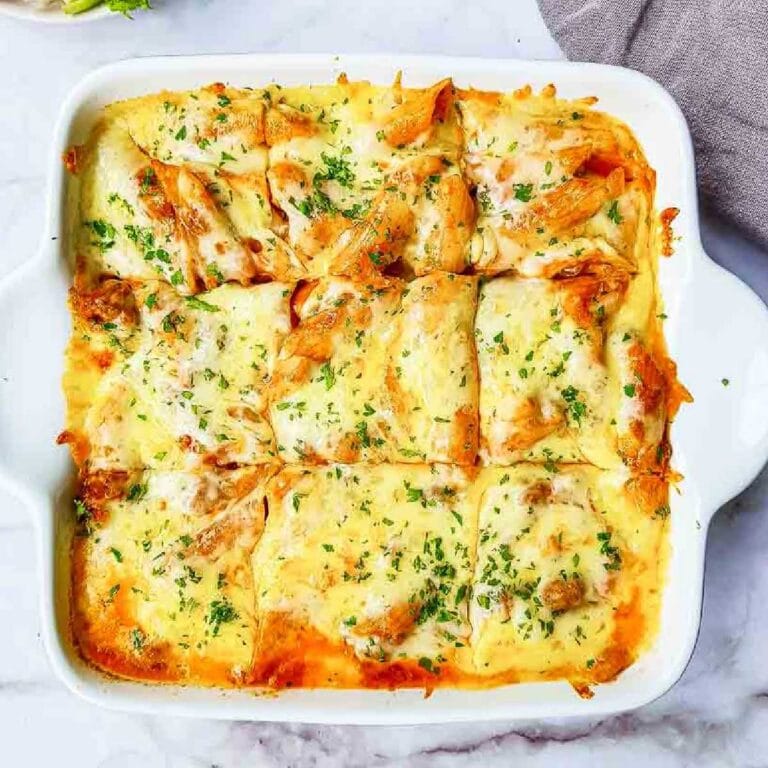 Top view of cheesy penne pasta bake sliced into squares in a white square baking dish.