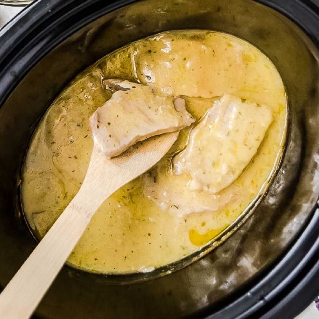 Cooked ranch pork chops in a crockpot with a wooden spoon.