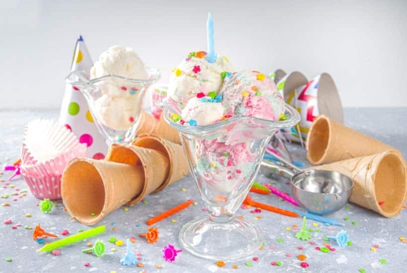 Sundae glasses filled with ice cream and surrounded by cones, candles and sprinkles.