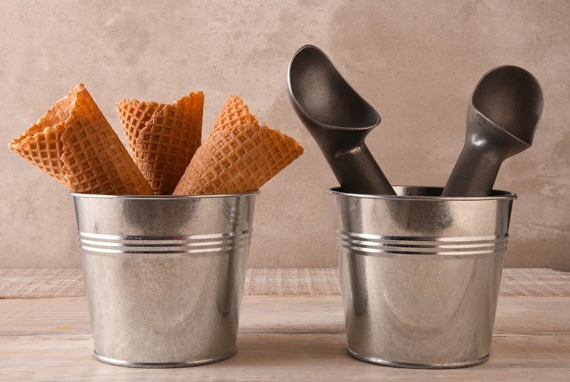 Two metal buckets filled with waffle cones and ice cream scoops.