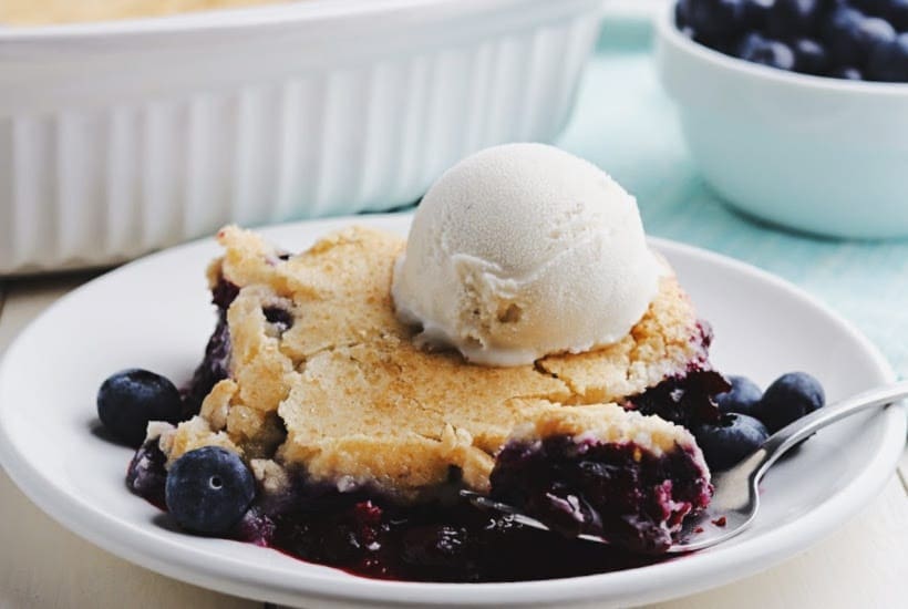 A slice of fruit cobbler and a scoop of vanilla ice cream on a white plate.