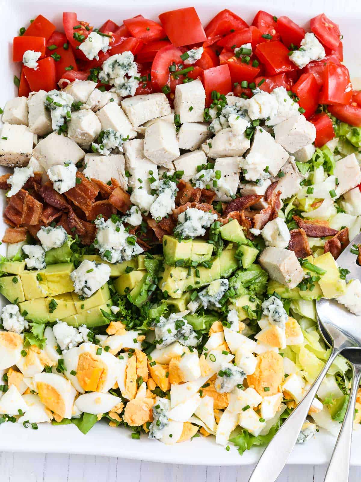 A layered cobb salad with veggies, cheese and chicken.