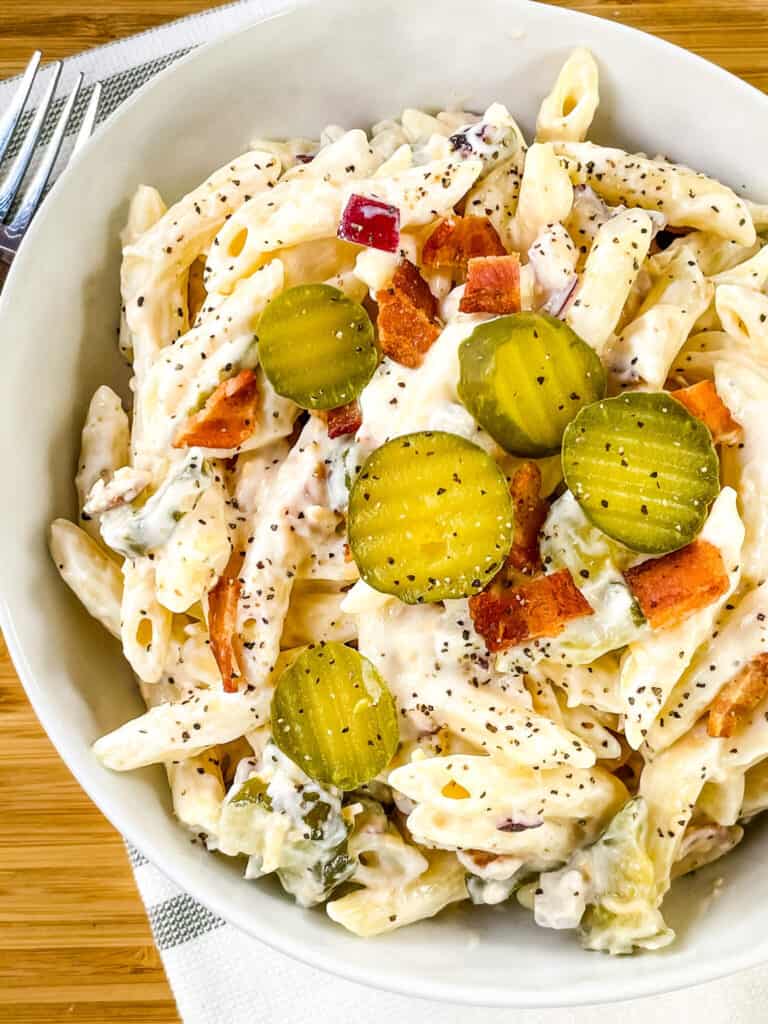 Pasta salad topped with bacon and pickle slices.