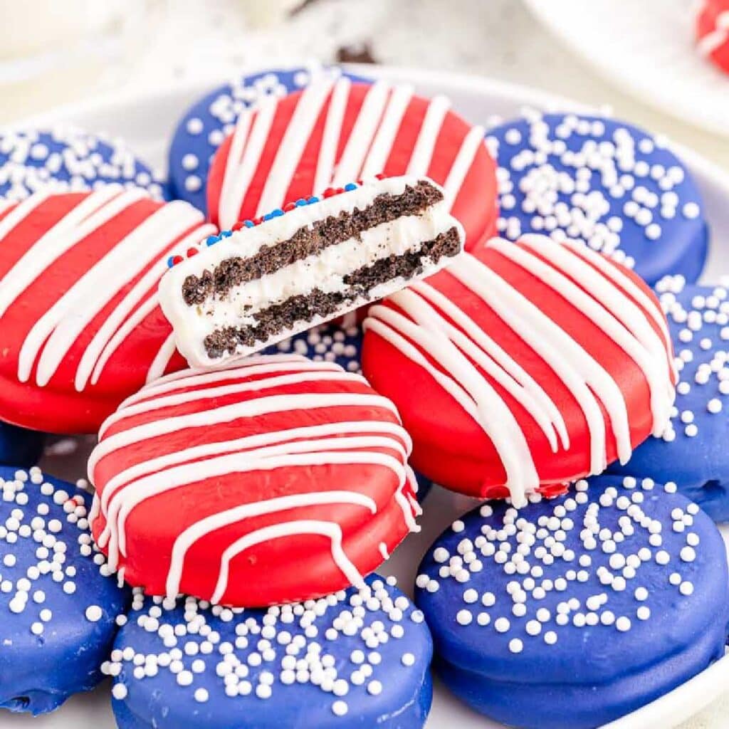 A white plate filled with red, white and blue chocolate covered Oreo cookies.