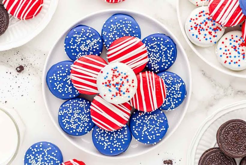 Chocolate dipped sandwich cookies decorated in patriotic red, white and blue colors on a white plate.