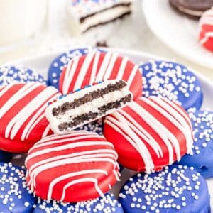 A plate of patriotic themed red, white and blue coated sandwich cookies with sprinkles and drizzle.