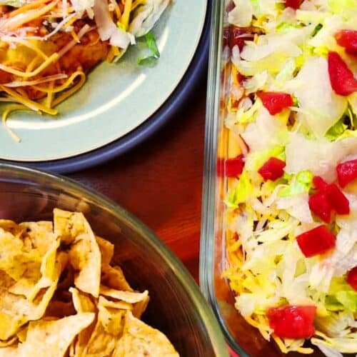 A casserole with 7 layer dip, and chips nearby.