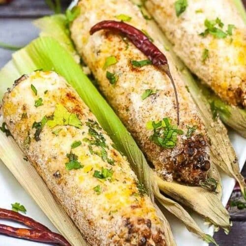 ears of Mexican street corn on a plate, coated with cheese.