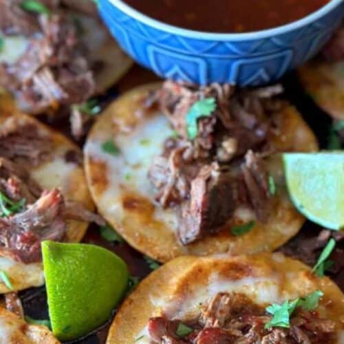 A spread of birria tacos with lime wedges.