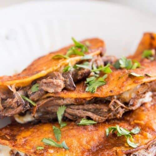 A plate of birria tacos with herbs over top.