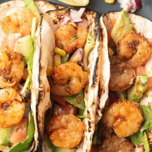 Three shrimp tacos with cabbage and avocado over top.