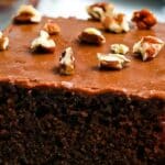 A slice of chocolate cake with a fudgy topping and walnuts.