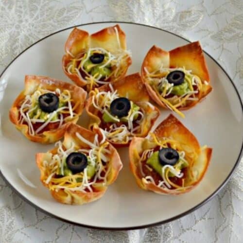 a plate of crispy taco cups with hummus, guacamole, and olives.