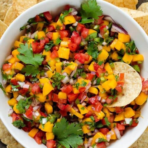 A bowl of colorful mango pico de gallo with chips around.