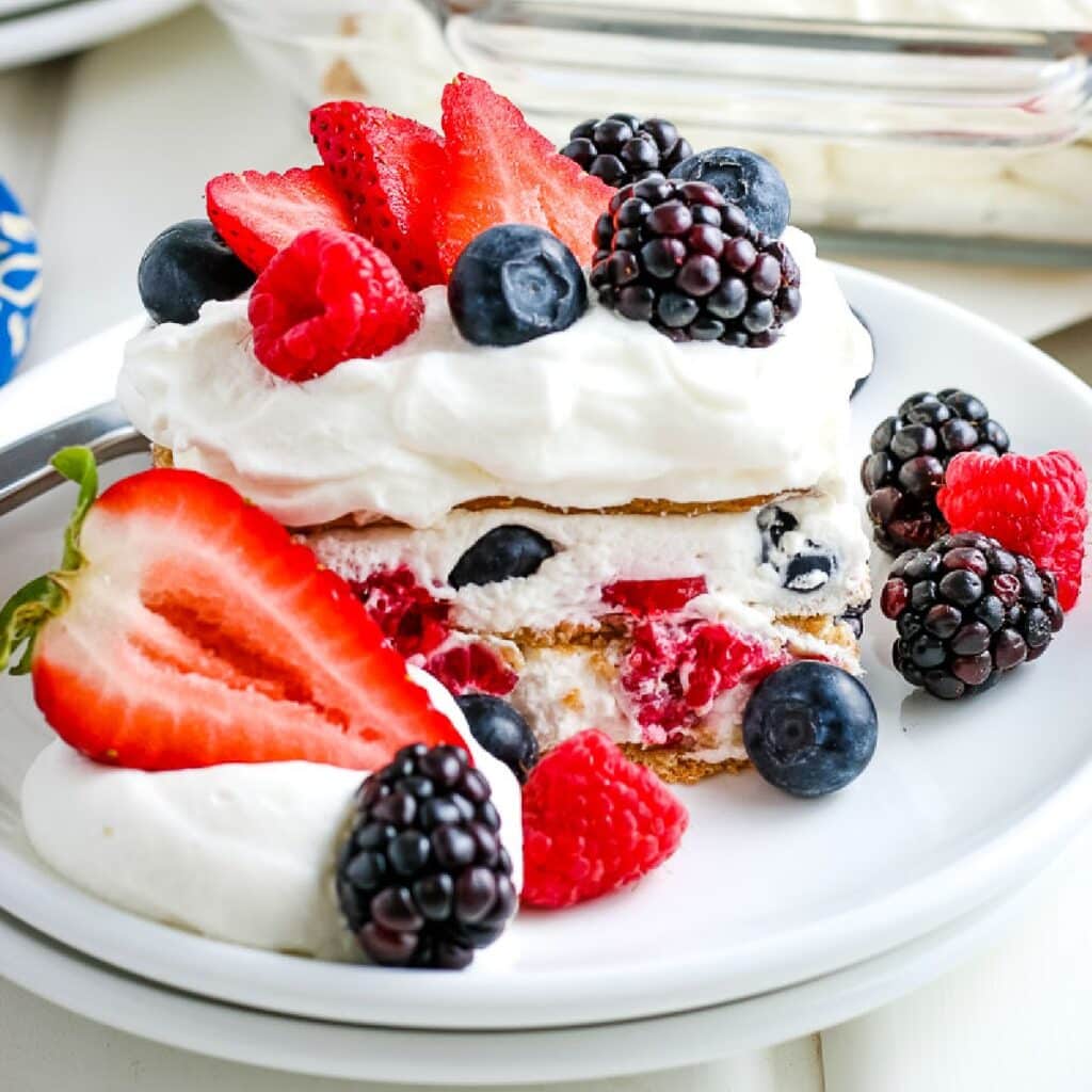 A slice of summer berry icebox cake on a white plate and garnished with fresh berries.