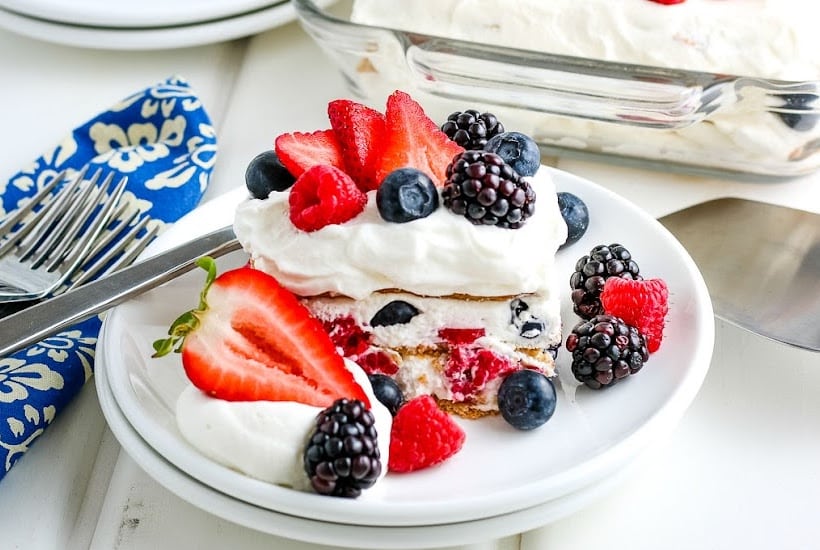 A slice of no bake icebox cake garnished with fresh berries on a white plate with a napkin and silverware to the side.