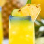 A glass of pineapple agua fresca with a pineapple chunk on the rim.