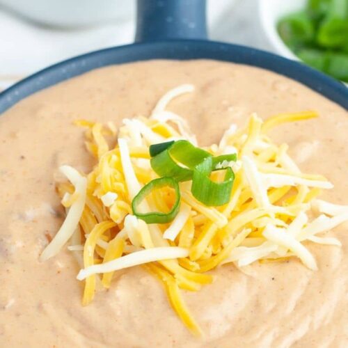 A bowl of creamy bean dip with cheese and peppers over top.