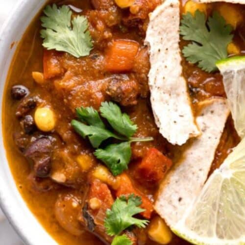 A bowl of meatless taco soup with beans and lime wedges.