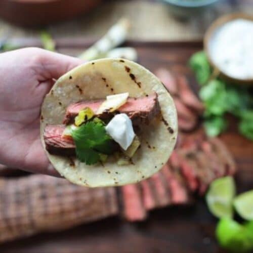 A hand holding a mini taco shell with skirt steak tacos.