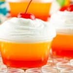 Layered jello shots with whipped cream and a cherry on top.