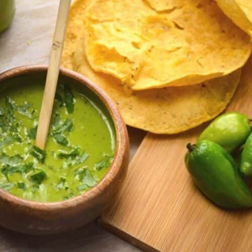 A bowl of homemade tomatillo hot sauce with tortillas near.