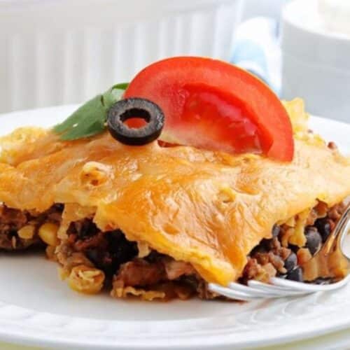 A slice of walking taco casserole on a plate, with olives and tomatoes on top.