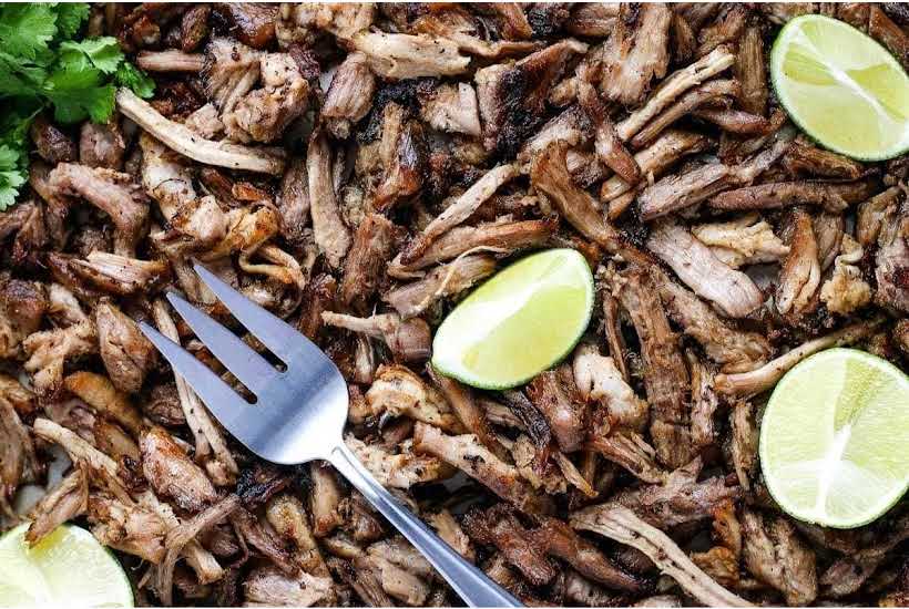 Closeup of pork carnitas meat with a fork and garnished with lime wedges.