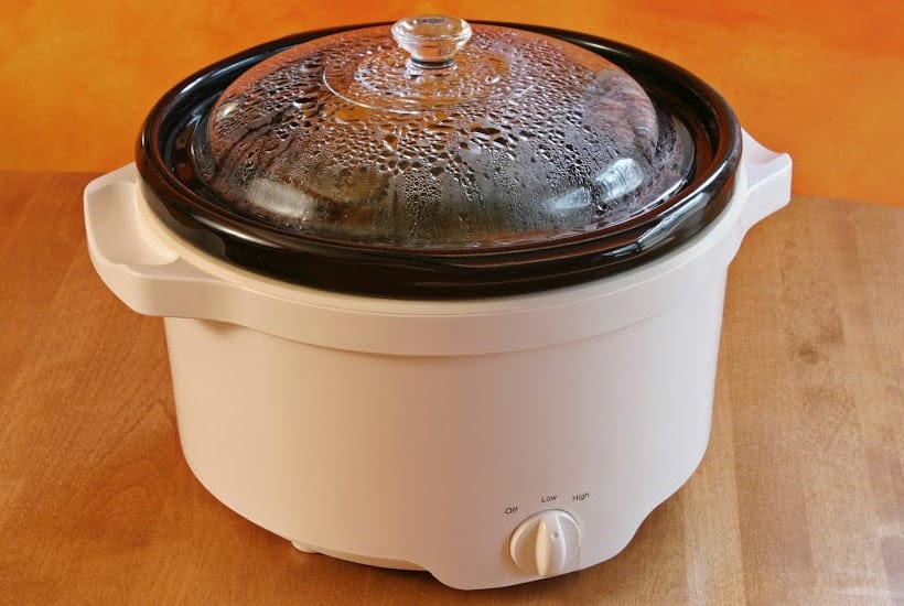 White slow cooker with glass lid on a wood counter top.