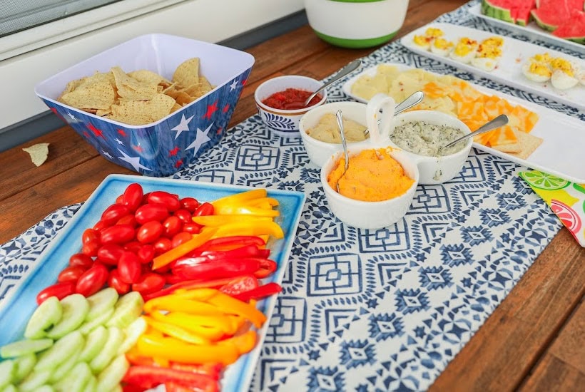 Serving table filled with vegetables, chips, and dips.