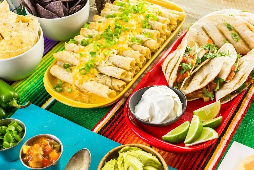 Table filled with trays of tacos and bowls of chips and sauces.