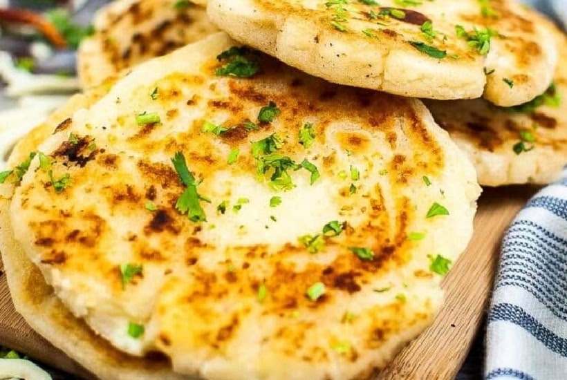 Arepas con queso garnished with parsley and piled on a wooden serving board.