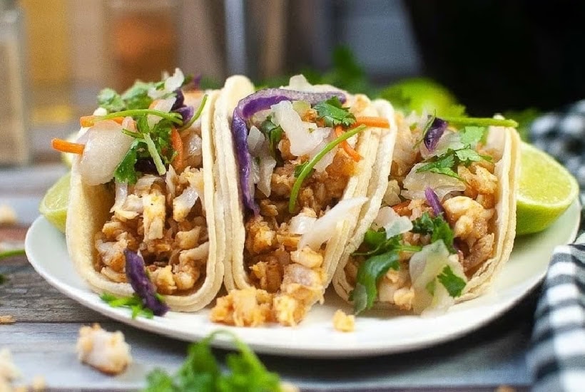 Three tilapia fish tacos on a white plate.