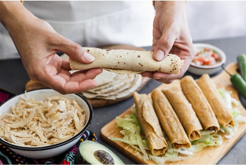 Making taquitos with shredded chicken and hands holding a rolled taquito.