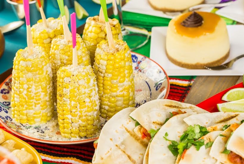 Plate of grilled corn on the cob, quesadilla wedges with a flan dessert in the background.