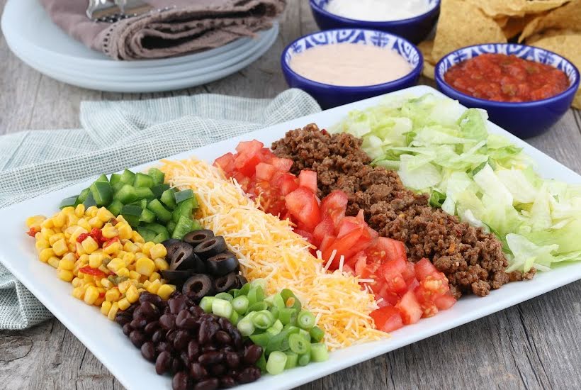 White serving tray filled with taco fillings and toppings with bowls of sauces in the background.