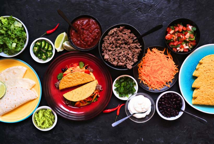 Table filled with tacos, toppings and fillings.