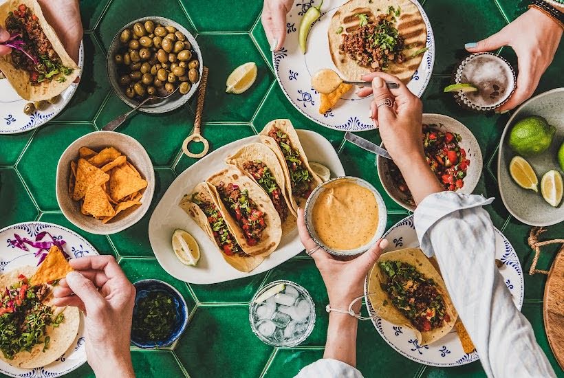 Green table filled with tacos, chips, side dishes and sauces.