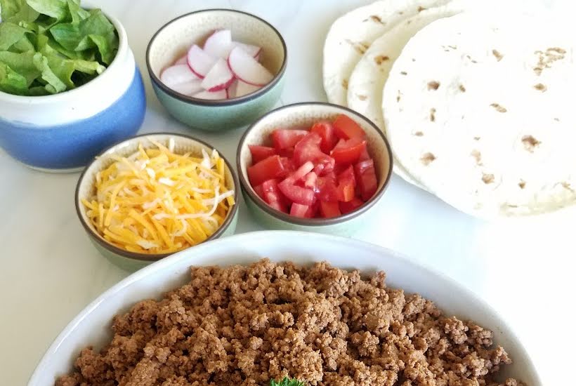 Bowls of taco meat and toppings with a stack of tortillas set up for a taco bar.