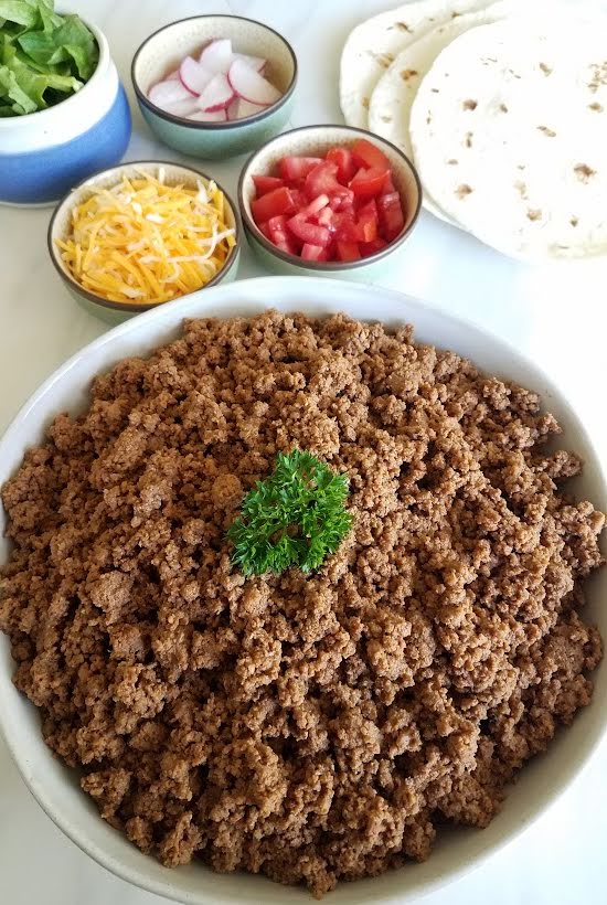 Large bowl of taco meat with smaller bowls of toppings.