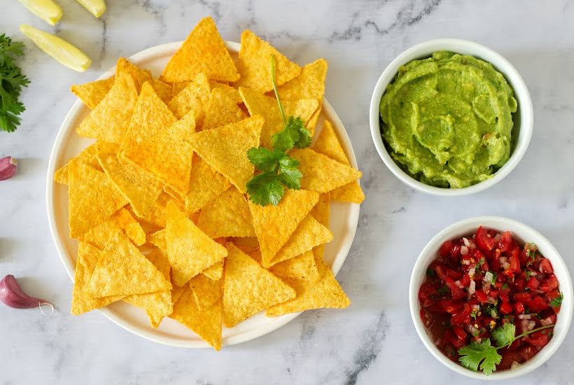 Bowl of tortilla chips with sides of salsa and guacamole.