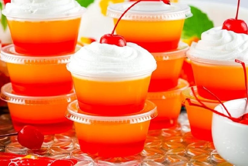 Stacks of tequila sunrise jello shots garnished with whipped cream and cherries.