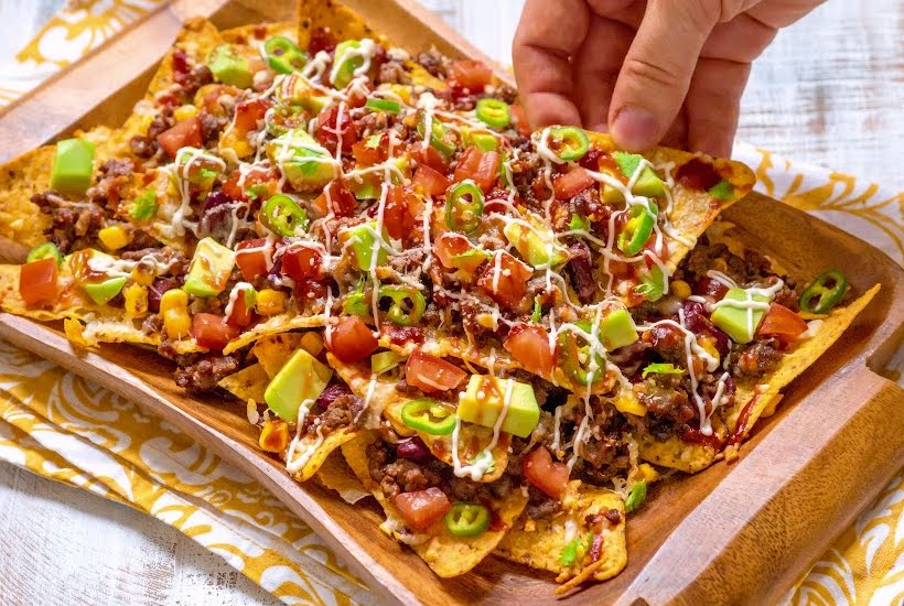 Loaded nachos on a wooden serving tray.