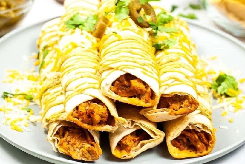 Plate of taquitos garnished with sauce, cheese and cilantro.