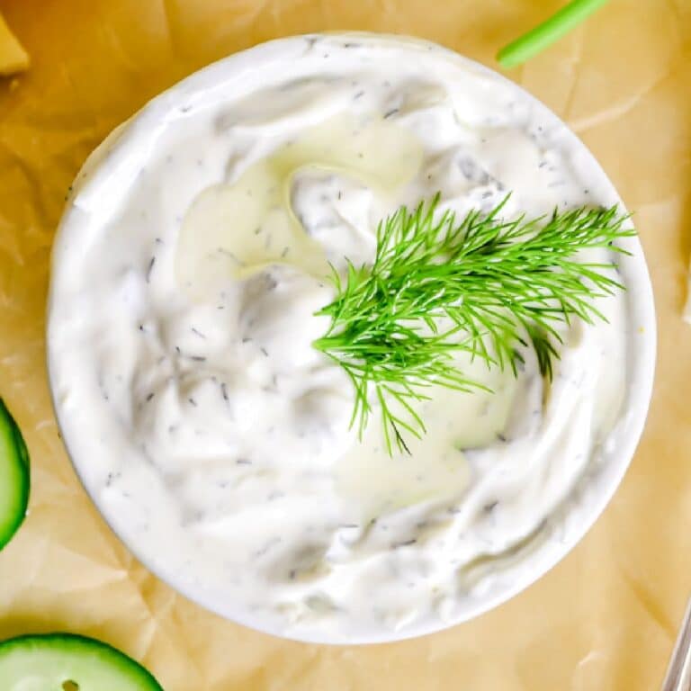 White bowl filled with creamy homemade tzatziki sauce and garnished with a sprig of fresh dill.